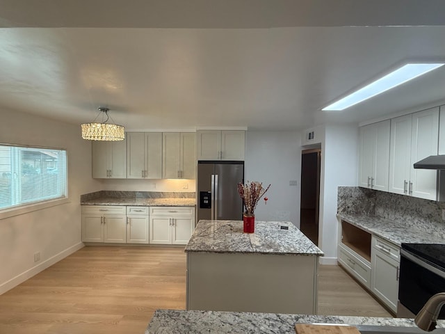 kitchen featuring light stone counters, pendant lighting, range with electric stovetop, a kitchen island, and stainless steel fridge