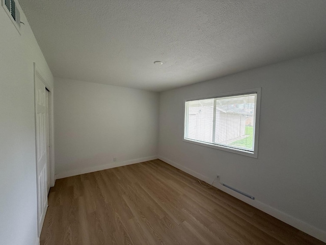 unfurnished room featuring a textured ceiling, baseboards, visible vents, and light wood-style floors