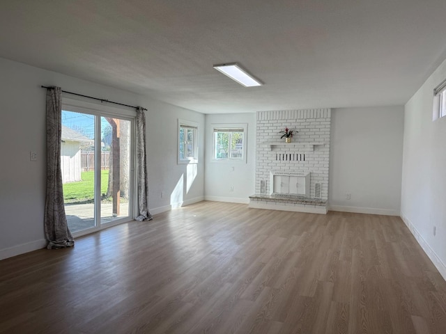 unfurnished living room with plenty of natural light, a fireplace, baseboards, and wood finished floors