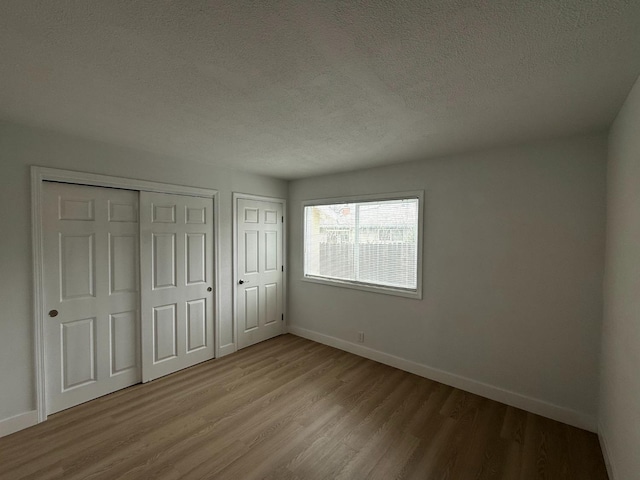 unfurnished bedroom with a textured ceiling, light wood-type flooring, two closets, and baseboards