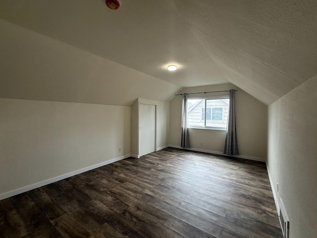 bonus room with dark wood-style floors, lofted ceiling, a textured ceiling, and baseboards