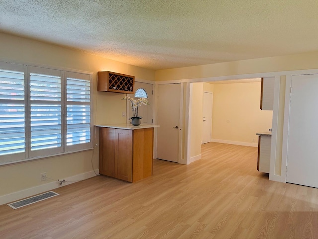 kitchen featuring a peninsula, visible vents, light wood-style floors, light countertops, and brown cabinets