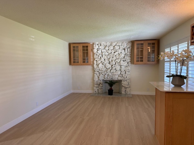 interior space with a textured ceiling, light wood finished floors, a fireplace, and baseboards