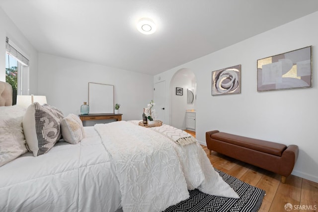 bedroom featuring arched walkways, wood finished floors, baseboards, and connected bathroom