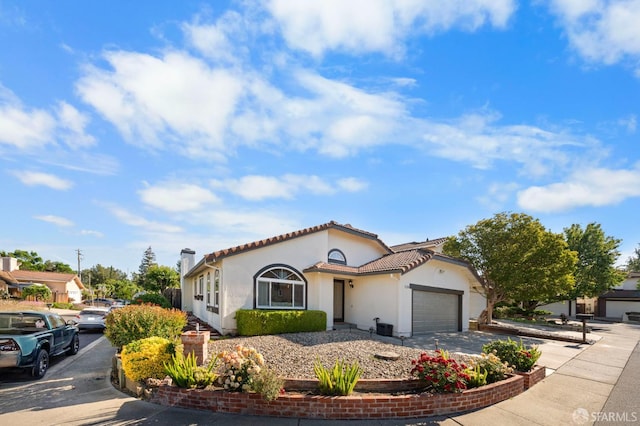mediterranean / spanish house featuring asphalt driveway, stucco siding, an attached garage, a tile roof, and a chimney