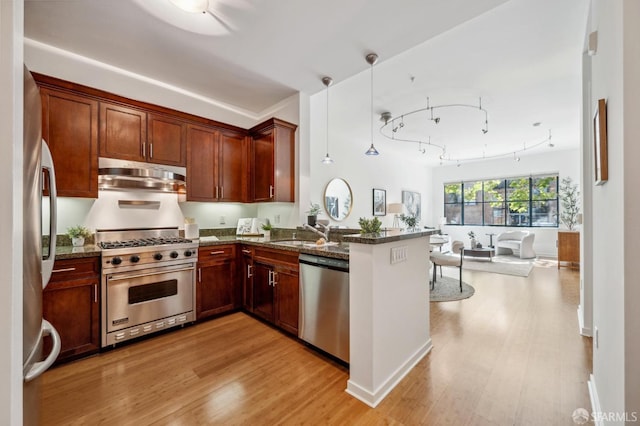 kitchen featuring appliances with stainless steel finishes, kitchen peninsula, light wood-type flooring, decorative light fixtures, and dark stone counters