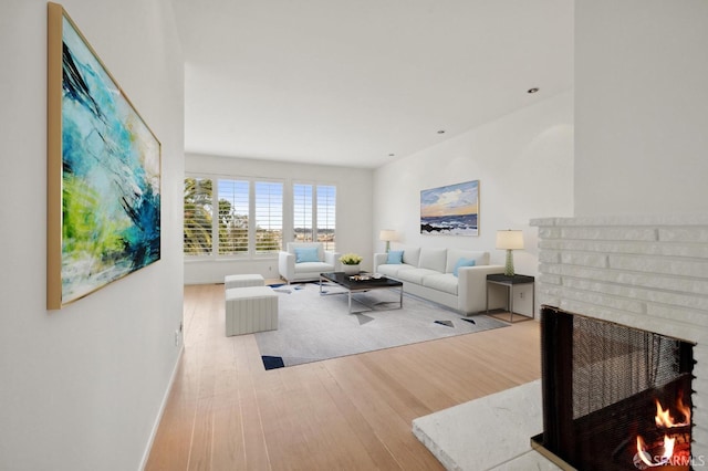 living room featuring a brick fireplace, baseboards, and wood finished floors