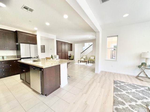 kitchen featuring sink, stainless steel appliances, dark brown cabinetry, a breakfast bar area, and a kitchen island with sink