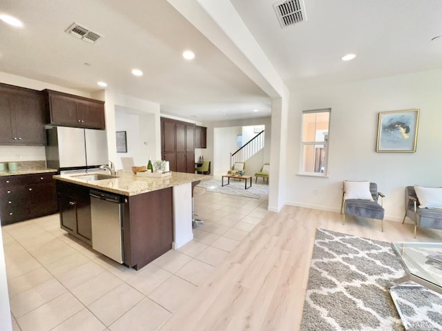 kitchen with a kitchen island with sink, a breakfast bar area, sink, stainless steel dishwasher, and light hardwood / wood-style floors