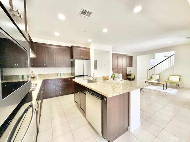 kitchen featuring a kitchen island with sink, light tile patterned flooring, sink, dark brown cabinetry, and stainless steel appliances