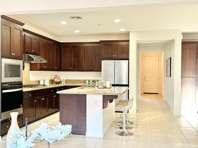 kitchen featuring light stone counters, an island with sink, dark brown cabinetry, and light tile patterned flooring