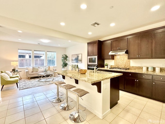 kitchen with a kitchen island with sink, a breakfast bar, light wood-type flooring, appliances with stainless steel finishes, and light stone counters