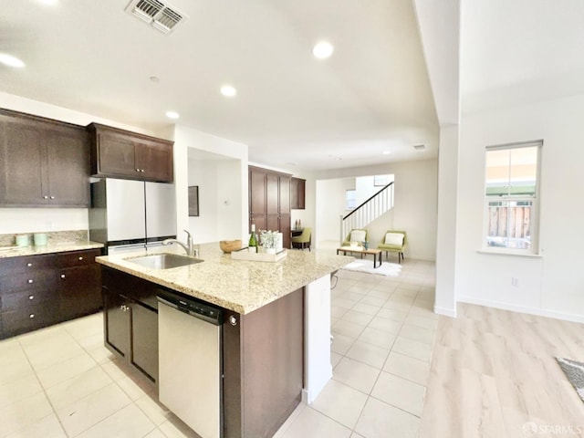 kitchen featuring a center island with sink, sink, light stone countertops, white refrigerator, and stainless steel dishwasher