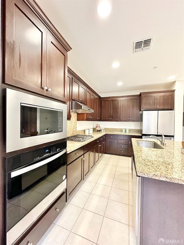 kitchen with appliances with stainless steel finishes, light stone counters, dark brown cabinets, and light tile patterned floors