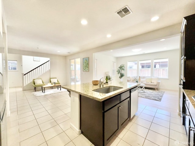 kitchen with a center island with sink, sink, light tile patterned floors, stainless steel dishwasher, and light stone counters