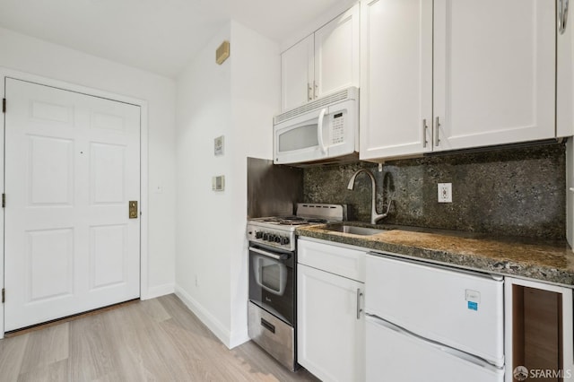 kitchen featuring sink, dark stone counters, white appliances, decorative backsplash, and white cabinets