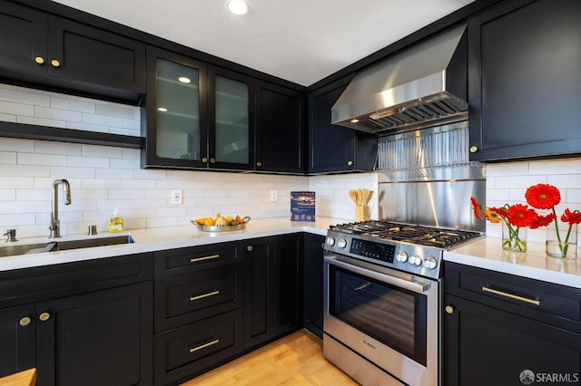 kitchen featuring sink, wall chimney range hood, light hardwood / wood-style flooring, tasteful backsplash, and stainless steel range with gas cooktop