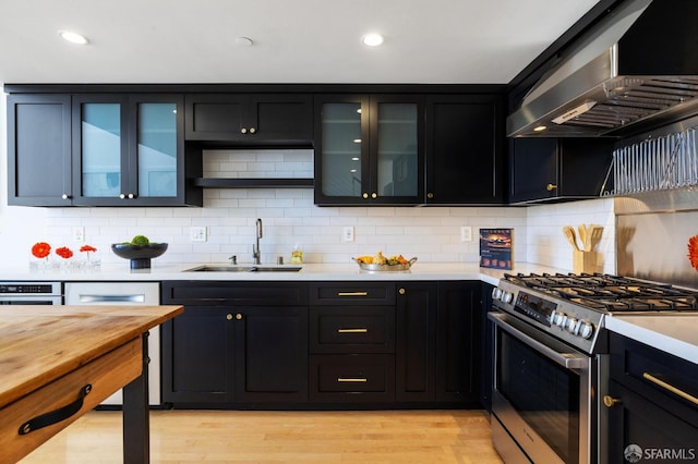 kitchen with wall chimney range hood, sink, stainless steel range with gas stovetop, decorative backsplash, and light wood-type flooring