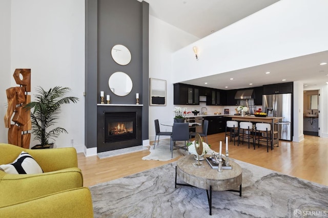 living room with a towering ceiling, sink, a large fireplace, and light hardwood / wood-style floors