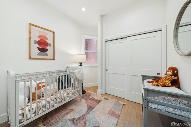 bedroom with a nursery area, light hardwood / wood-style floors, and a closet