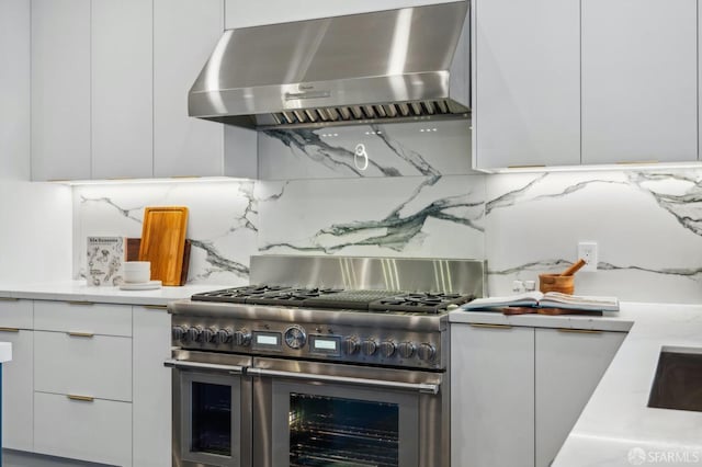 kitchen featuring white cabinetry, ventilation hood, range with two ovens, and backsplash