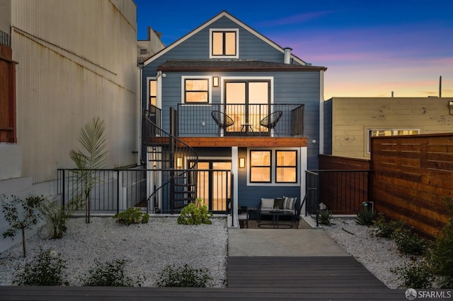 back house at dusk with a balcony, outdoor lounge area, and a patio