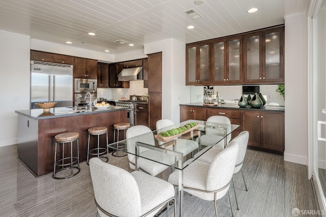 kitchen featuring visible vents, dark countertops, built in appliances, under cabinet range hood, and a sink