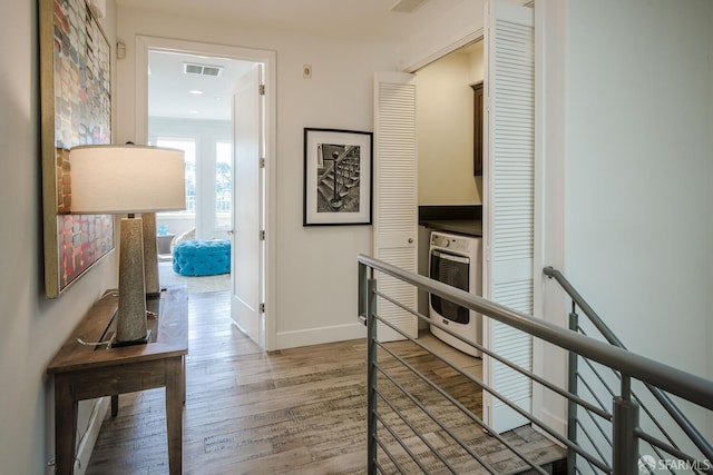 corridor with light wood-type flooring, baseboards, visible vents, and an upstairs landing