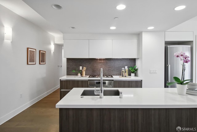 kitchen featuring dark wood-type flooring, white cabinets, decorative backsplash, a kitchen island with sink, and appliances with stainless steel finishes