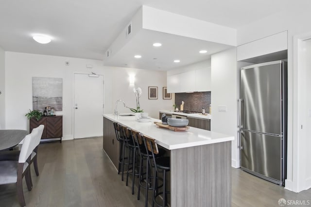 kitchen featuring wood-type flooring, stainless steel appliances, white cabinetry, a breakfast bar area, and a kitchen island with sink