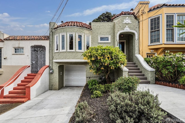 mediterranean / spanish house with a garage, a tile roof, driveway, and stucco siding