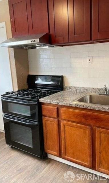 kitchen featuring black range with gas stovetop, decorative backsplash, light stone counters, and light hardwood / wood-style floors