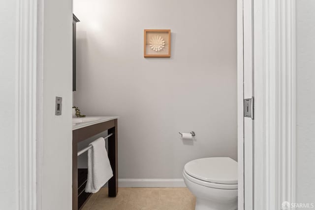 half bath with vanity, tile patterned floors, toilet, and baseboards