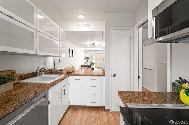 kitchen featuring stainless steel appliances, a sink, light wood-style floors, white cabinetry, and glass insert cabinets