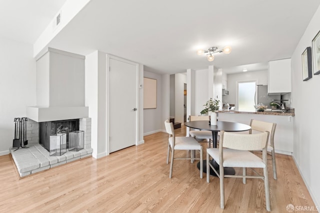 dining room featuring light wood finished floors, baseboards, and a brick fireplace