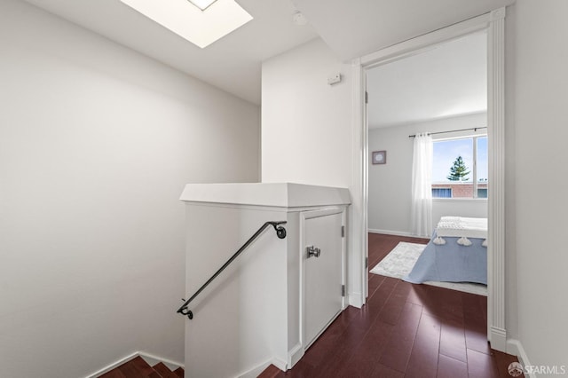hall featuring an upstairs landing, a skylight, dark wood finished floors, and baseboards