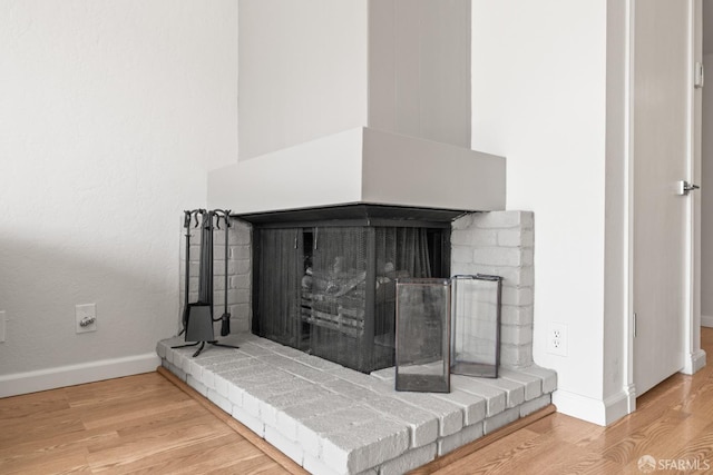 detailed view of a brick fireplace, wood finished floors, and baseboards