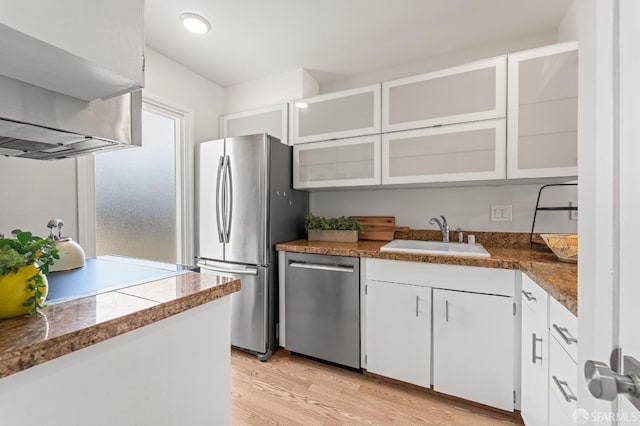kitchen featuring stainless steel appliances, a sink, light wood-style floors, white cabinets, and extractor fan