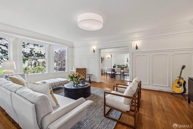 living room with wood finished floors, crown molding, and a decorative wall