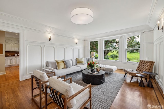 living room with crown molding, a decorative wall, and light wood-style floors