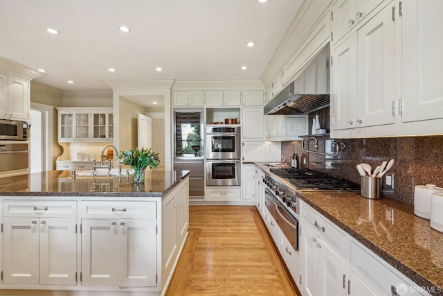 kitchen featuring white cabinetry, wall chimney exhaust hood, appliances with stainless steel finishes, and a sink