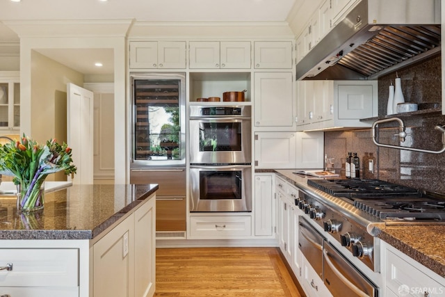 kitchen featuring light wood finished floors, stainless steel double oven, stovetop, under cabinet range hood, and backsplash