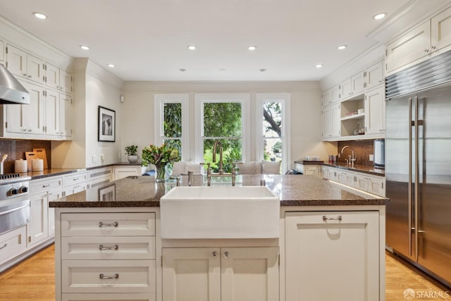 kitchen with dark stone countertops, light wood-style flooring, a sink, ornamental molding, and built in refrigerator