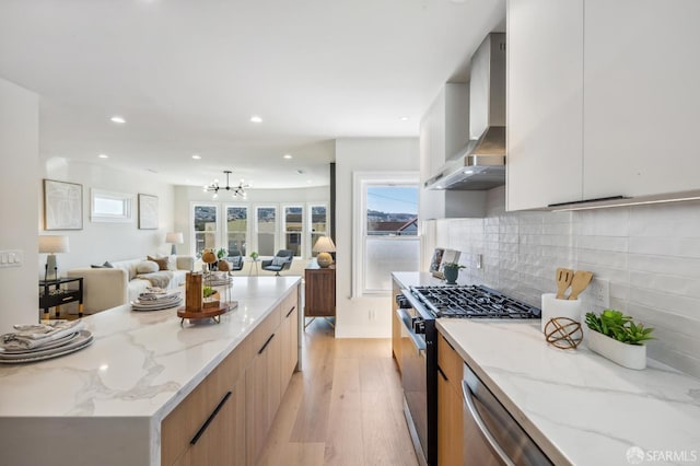 kitchen featuring white cabinetry, appliances with stainless steel finishes, wall chimney exhaust hood, and light stone countertops