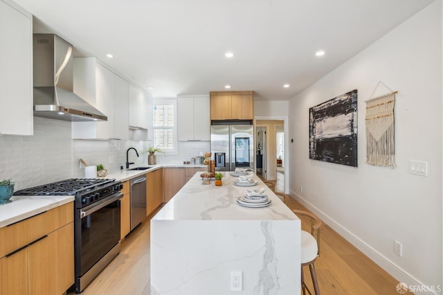 kitchen featuring wall chimney range hood, sink, appliances with stainless steel finishes, white cabinetry, and a center island