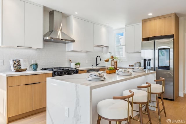 kitchen featuring a breakfast bar, white cabinetry, stainless steel fridge with ice dispenser, a kitchen island, and wall chimney range hood