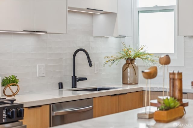 kitchen featuring dishwasher, white cabinetry, sink, decorative backsplash, and light stone counters