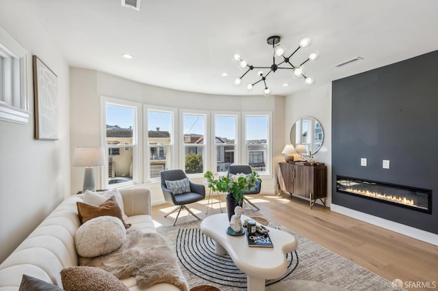 living room with an inviting chandelier, a large fireplace, and light hardwood / wood-style floors