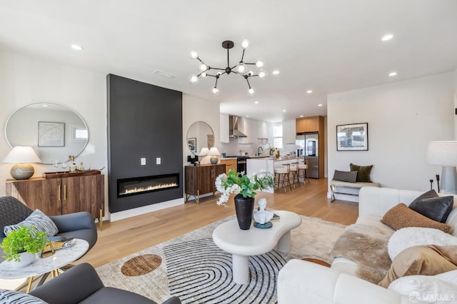 living room featuring an inviting chandelier, a large fireplace, sink, and light hardwood / wood-style floors