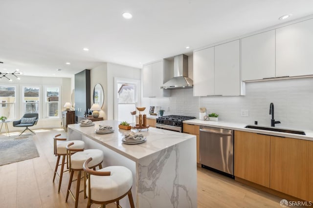 kitchen featuring sink, white cabinetry, a center island, stainless steel appliances, and wall chimney range hood